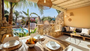 Eine sonnendurchflutete Terrasse mit Steinmauer, Pool und Essbereich mit Tisch für zwei Personen.