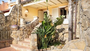 Eine Steintreppe führt zu einem Haus mit Balkon, umgeben von tropischen Pflanzen.