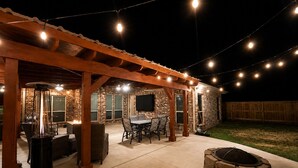 Un patio al aire libre con muro de ladrillo, zona de estar cubierta y luces colgantes.