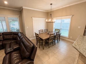 A dining area with a wooden table and chairs, a leather sofa, and a chandelier.