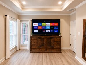 Ein Fernseher zeigt verschiedene Streaming-Apps und Sender, darunter ein Holzkasten und ein Fenster mit Jalousien links.