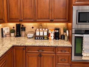 A kitchen with wooden cabinets, granite countertop, and stainless steel appliances including a coffee maker, toaster, and oven. - Best Patio in BCS/4.1 mi to Kyle Field/82” TVs/Fire Pit/Nursery (College Station)
