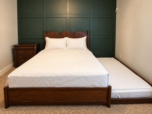 A single bed with a wooden frame and a white mattress in a room with a dark green wall and a small wooden nightstand.