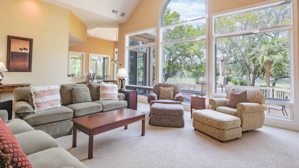 A spacious living room with a large window, a ceiling fan, and a cozy seating area. - 4 Minute Walk to Beach!  Private Pool With Pool Heater.*  Back Deck w/ Lagoon & Golf Course Views! (Hilton Head Island)