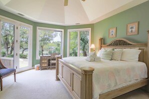 A bedroom with a large bed, a chair, a dresser, and a window overlooking a garden.