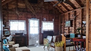 Interior rústic de fusta amb un sostre alt, un ventilador de sostre, un sofà, una taula de dinar i una catifes de quadres.