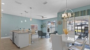 A modern kitchen with a central island, dining area with chairs, and a ceiling fan. - Lovely Family Home - 8 Min to Disney! (Kissimmee)
