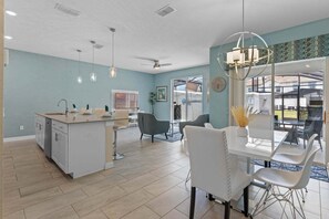 Une cuisine moderne dotée d’un îlot central, d’un coin repas avec des chaises blanches et d’un ventilateur de plafond.