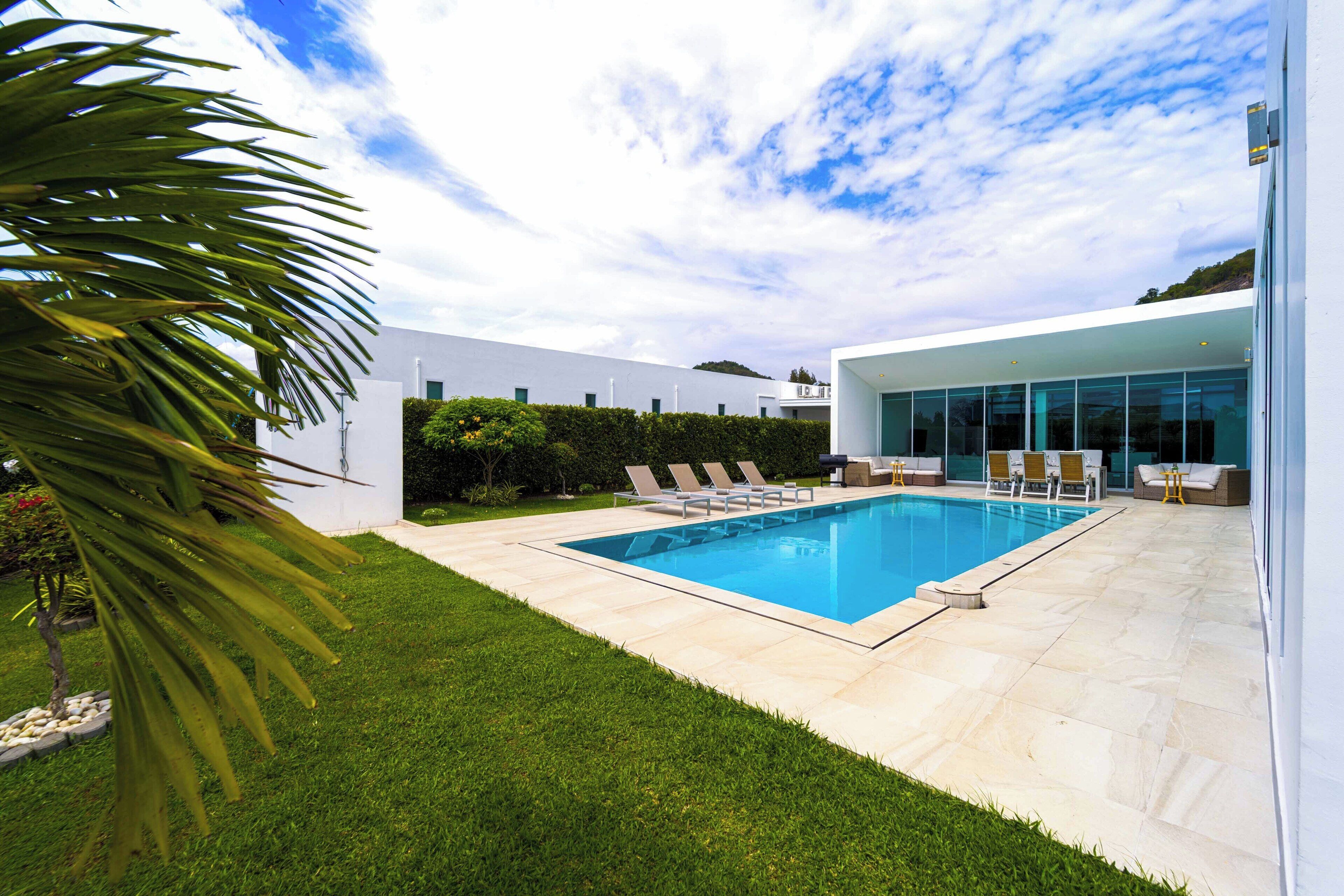A modern outdoor swimming pool with lounge chairs and a glass-enclosed building in the background.