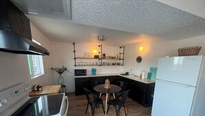Une cuisine compacte équipée d’une cuisinière, d’un four à micro-ondes et d’un réfrigérateur. On y trouve une table à manger avec des chaises, ainsi qu’un petit îlot central doté d’un évier.