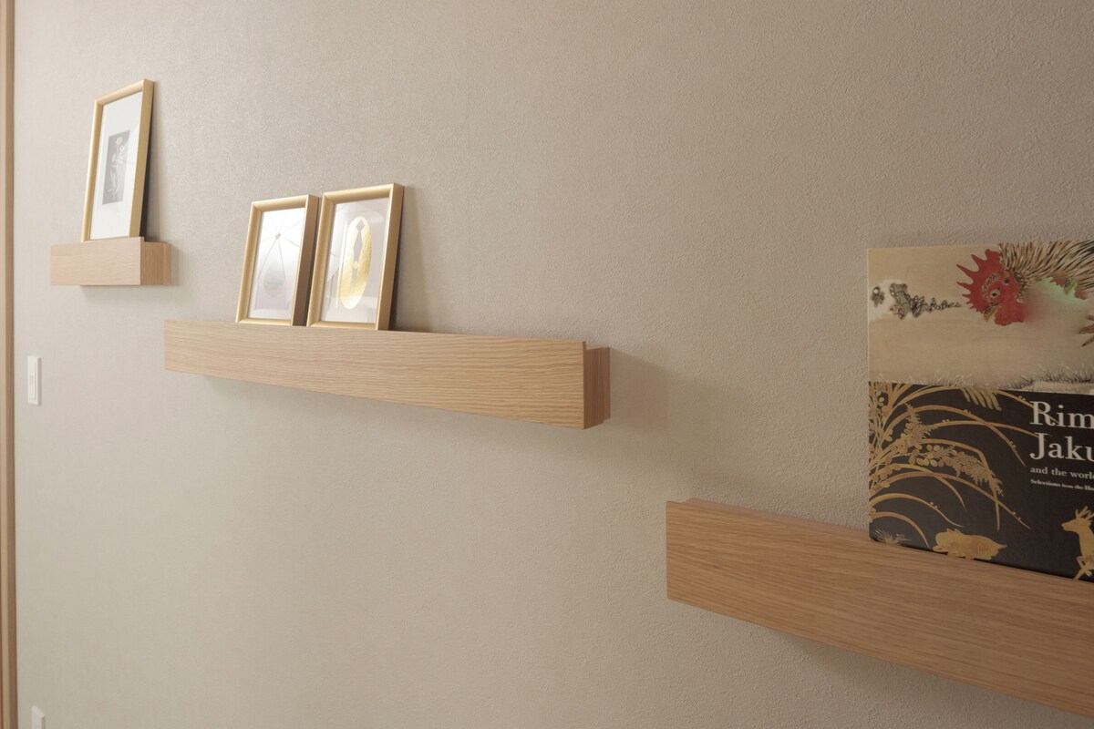 A wall with three wooden shelves, each holding framed pictures and a book.