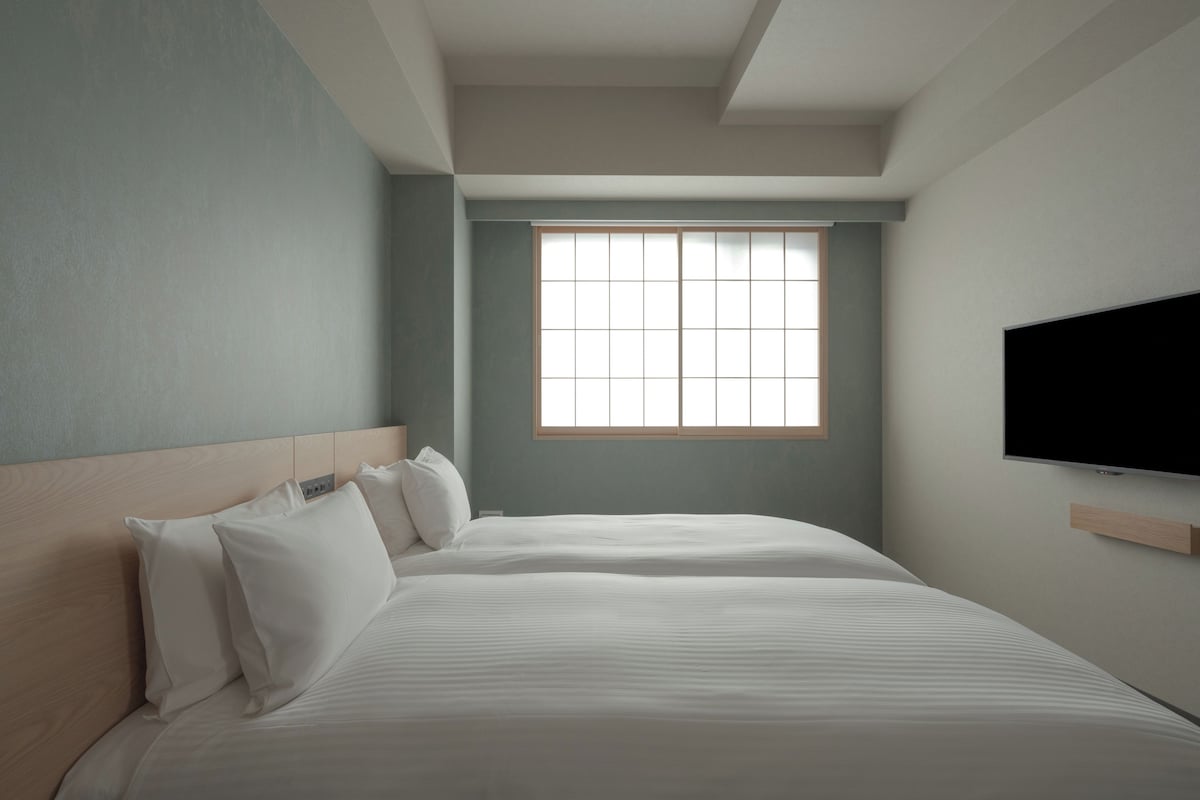 A hotel room with a large bed, a television mounted on the wall, and a window providing natural light.