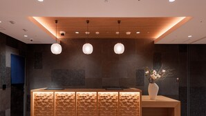 Una reception con finitura in legno e pannello posteriore strutturato, con un vaso di fiori e luci a sospensione.