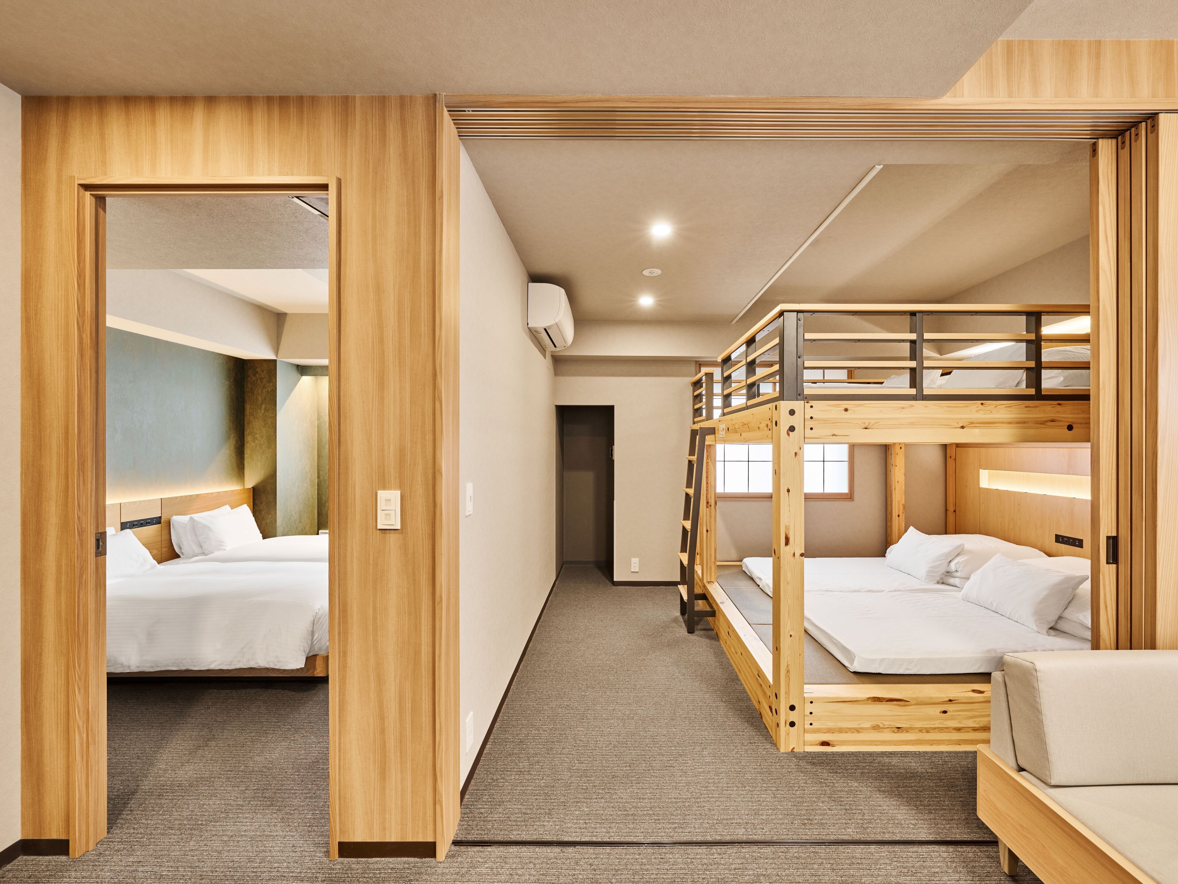 Una stanza con due letti, un letto a castello, una porta in legno e pavimento coperto da moquette.