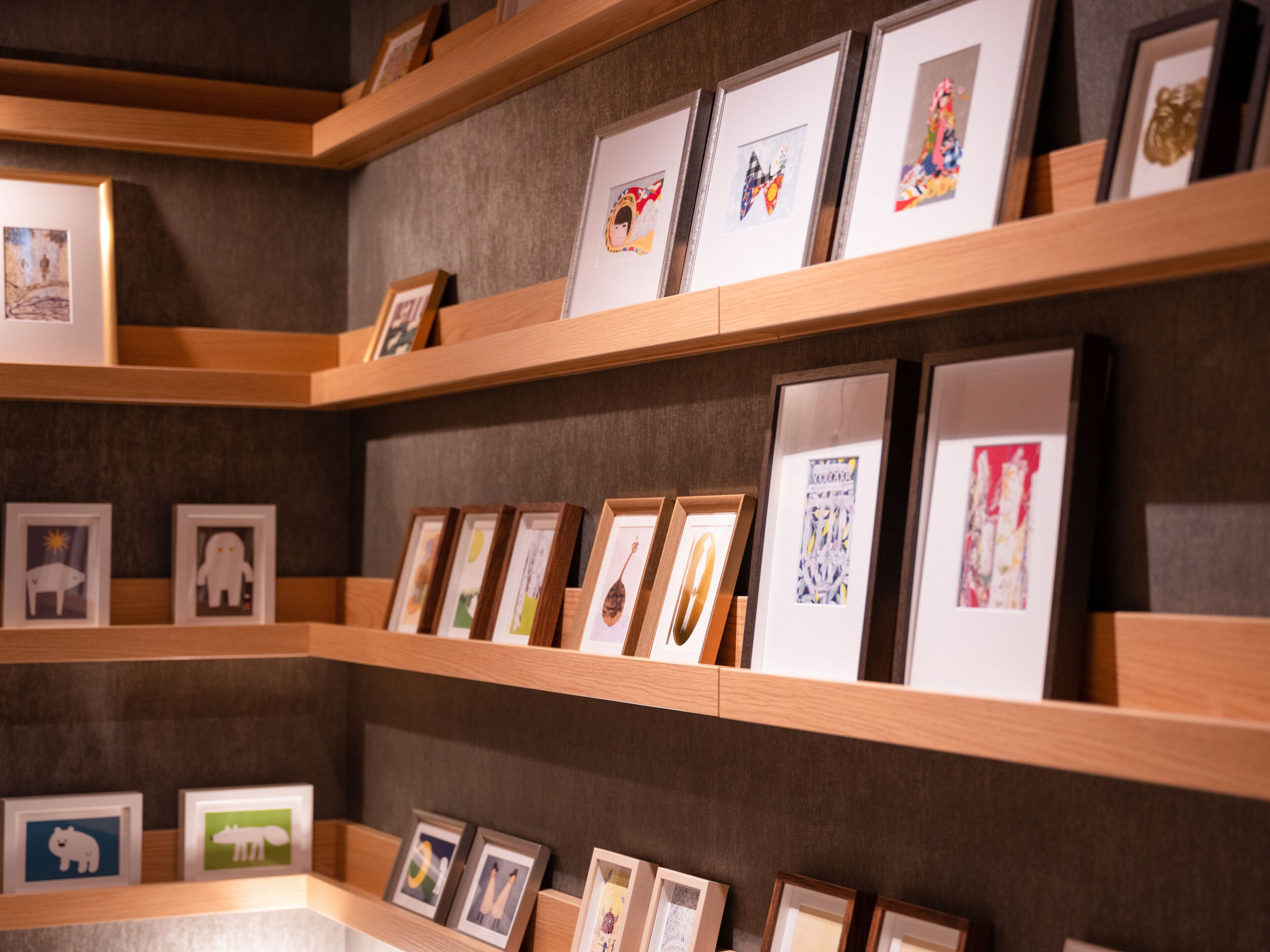 A gallery wall with framed artworks on wooden shelves.