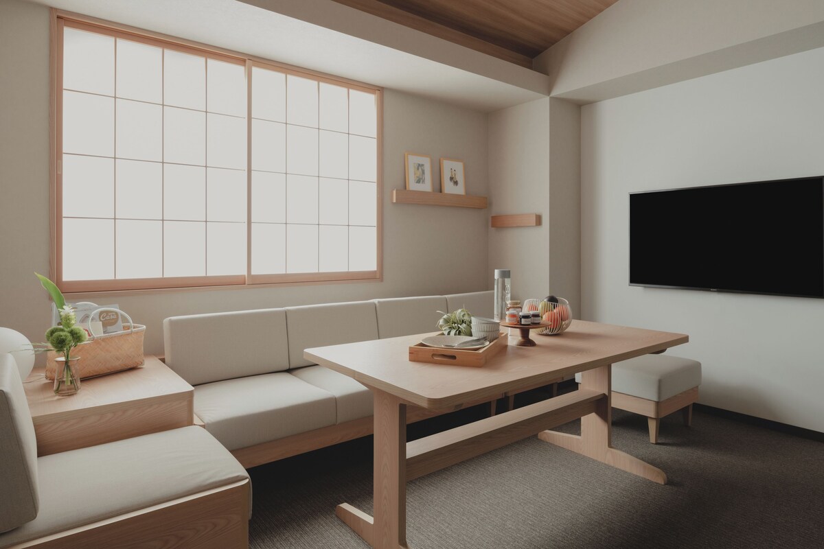 A modern living room with a wooden table, beige sofa, and a large window.