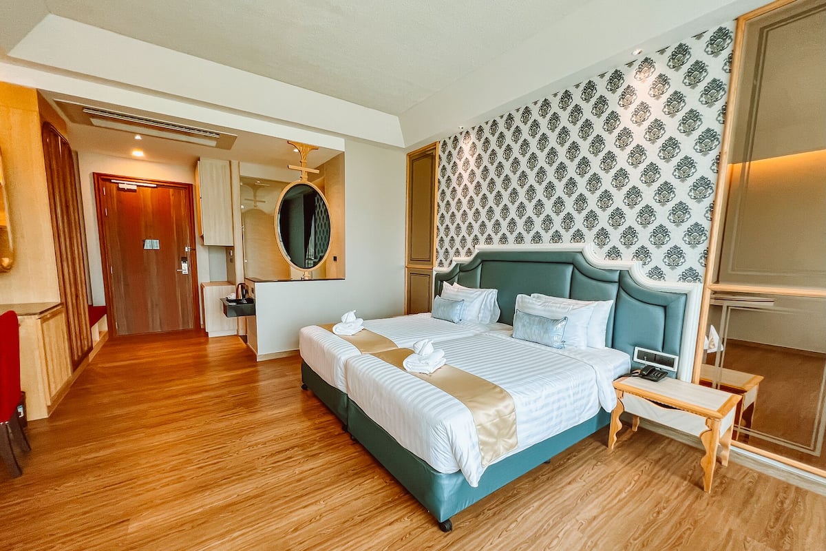 A hotel room with a large bed, a bedside table, a mirror, and a patterned wall.
