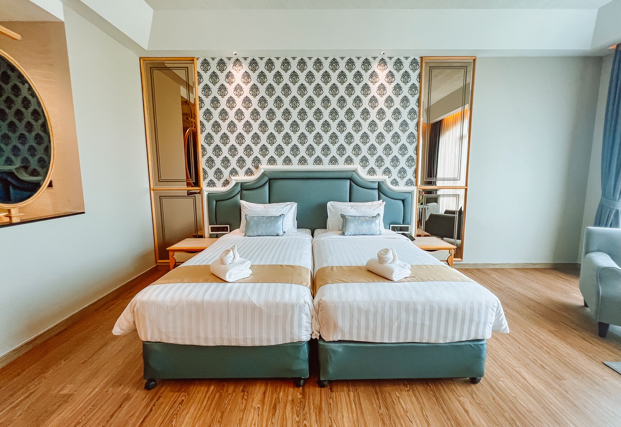 A hotel room with a large bed, two bedside tables, a mirror, and a patterned wallpaper.