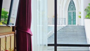 A view through a window with a red curtain, leading to a staircase and a building with a green door. - Grand Lord Hotel& Residence (Sattahip)