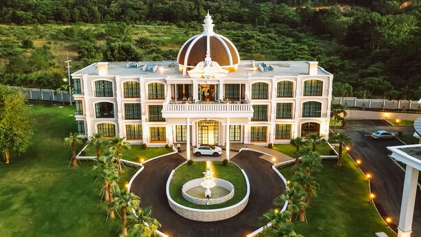 A large, white, multi-story building with a central dome, surrounded by a well-manicured lawn and palm trees. - Grand Lord Hotel& Residence (Sattahip)