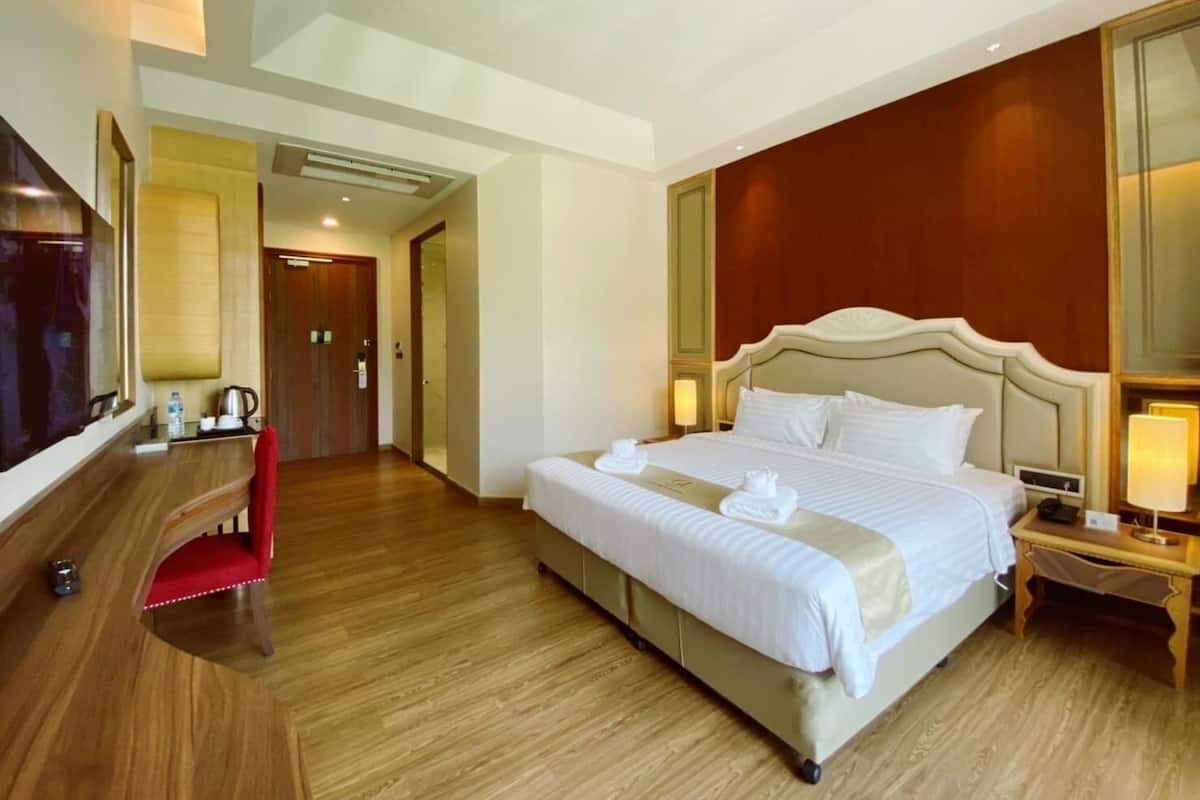 A hotel room with a large bed, a desk, a chair, a TV, and a mirror.