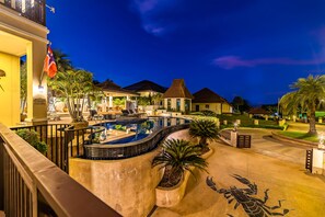 A resort with a swimming pool, palm trees, and a well-lit entrance.