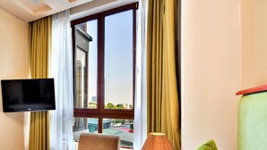 A hotel room with a bed, a chair, a TV mounted on the wall, a lamp, and a window with curtains. - HANZ LakeView Hotel Hanoi (Hanoi)