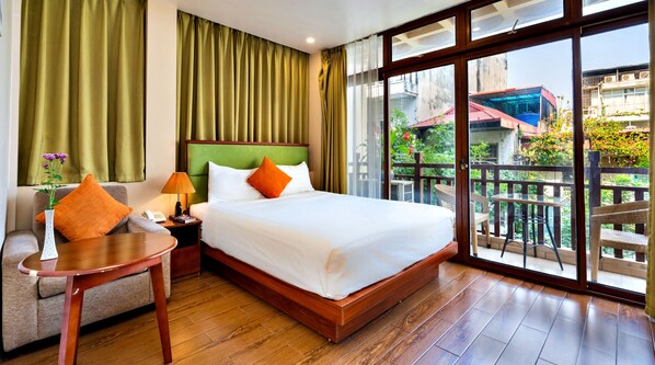 A hotel room with a bed, a small table, a chair, a nightstand, a lamp, and a view of the outside balcony. - HANZ LakeView Hotel Hanoi (Hanoi)