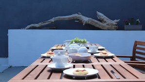 A wooden table set for a meal with white plates, bowls, and cups, against a blue wall with a large branch decoration. - A beautiful refurbished Cornish Cottage with BBQ & Patio (Falmouth)