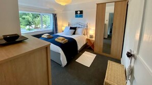 A bedroom with a bed, bedside tables, a window, and a door. - A beautiful refurbished Cornish Cottage with BBQ & Patio (Falmouth)