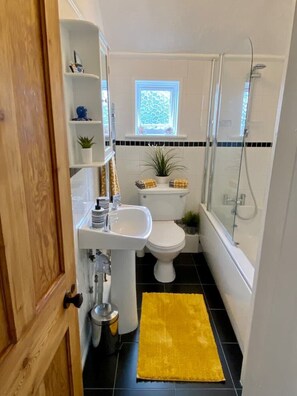 Bathroom features a sink, toilet, and shower area with a window above the toilet.