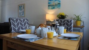 A breakfast table set with plates, glasses, and a croissant, with a lamp and a painting in the background. - A beautiful refurbished Cornish Cottage with BBQ & Patio (Falmouth)