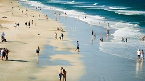 Ein Strand mit Menschen, die am Ufer entlanggehen, einem klaren Himmel und Wellen in der Ferne.