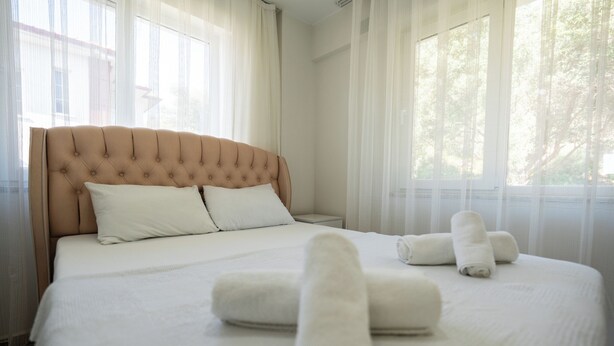 Una habitación de hotel con una cama grande, ropa de cama blanca y toallas enrolladas.