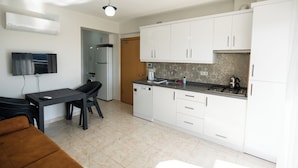 Una cocina compacta con armarios blancos, lavavajillas integrado, estufa y comedor con mesa y sillas.