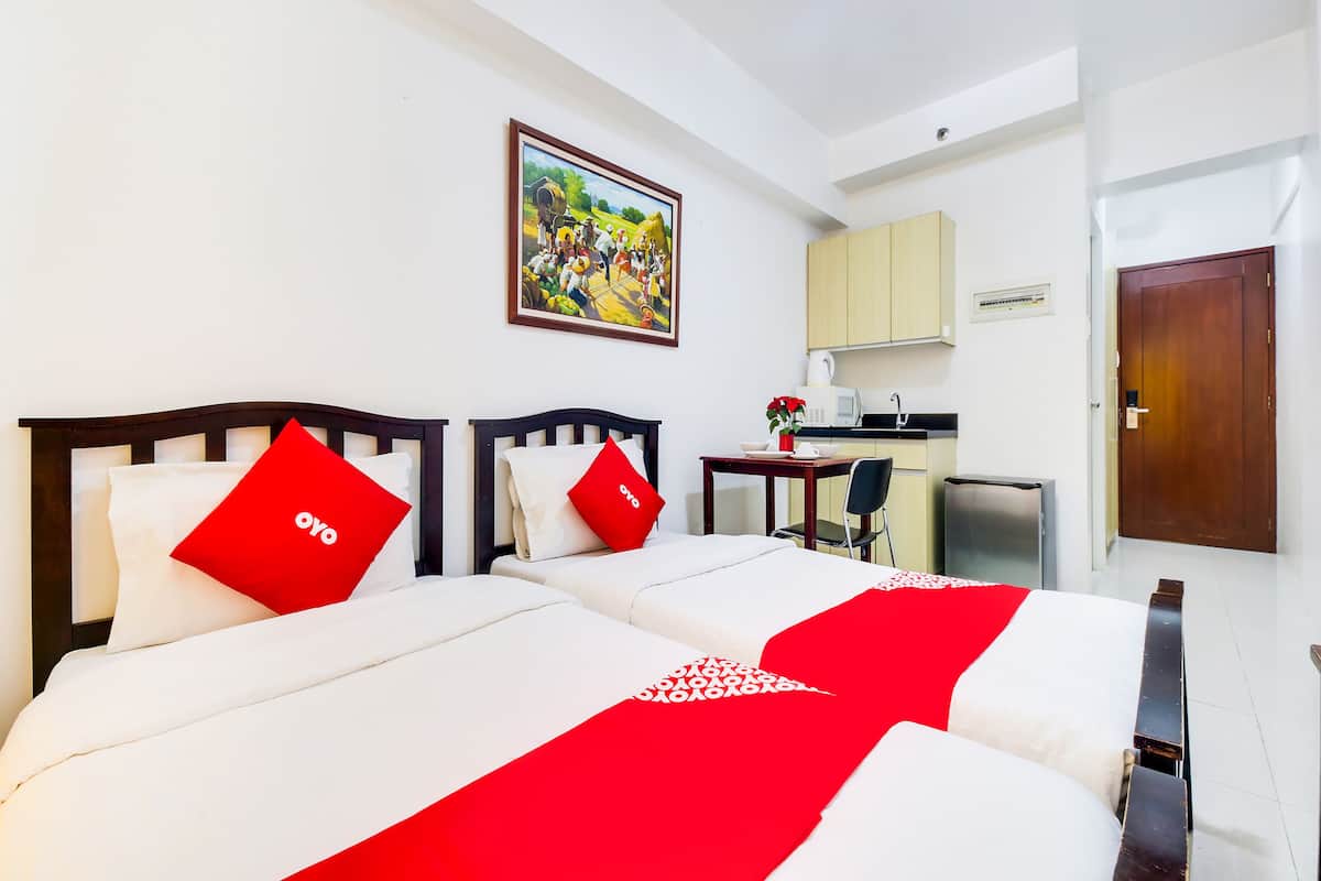 Habitación de hotel con dos camas, una kitchenette pequeña y una puerta.