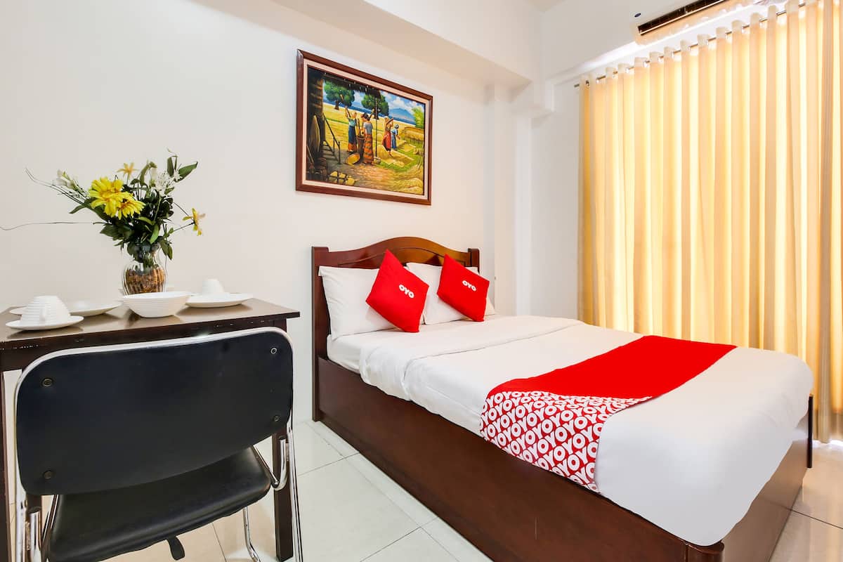 Habitación de hotel con una cama, un escritorio con una silla, un jarrón con flores y un cuadro en la pared.