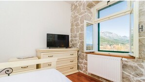 A bedroom with a stone wall, a bed, a dresser, a TV, and a window with a mountain view. - Quiet Village Villa (Desne)