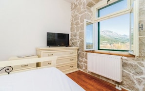A bedroom with a stone wall, a bed, a dresser, a TV, and a window with a mountain view.