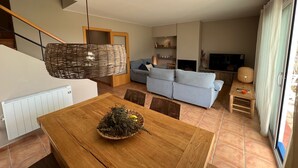 A modern living room with a sofa, a dining table with a centerpiece, a TV, and a staircase. - Les Dunes 4433 - 60m from the beach, pool and garden (Torroella de Montgri)