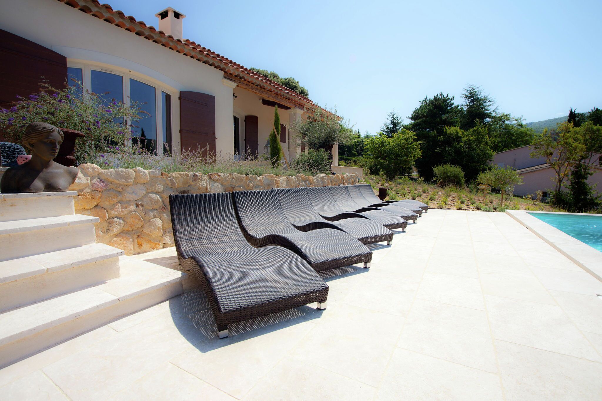 Un espace aménagé au bord de la piscine, avec des chaises longues, un mur en pierre et une statue.