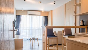 A modern kitchen with wooden cabinets, a bar stool, and a sofa. - ONE Hotel (Khlong Luang)