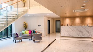 A modern hotel lobby with a marble reception desk, a staircase with glass railings, and a seating area with colorful cushions. - ONE Hotel (Khlong Luang)
