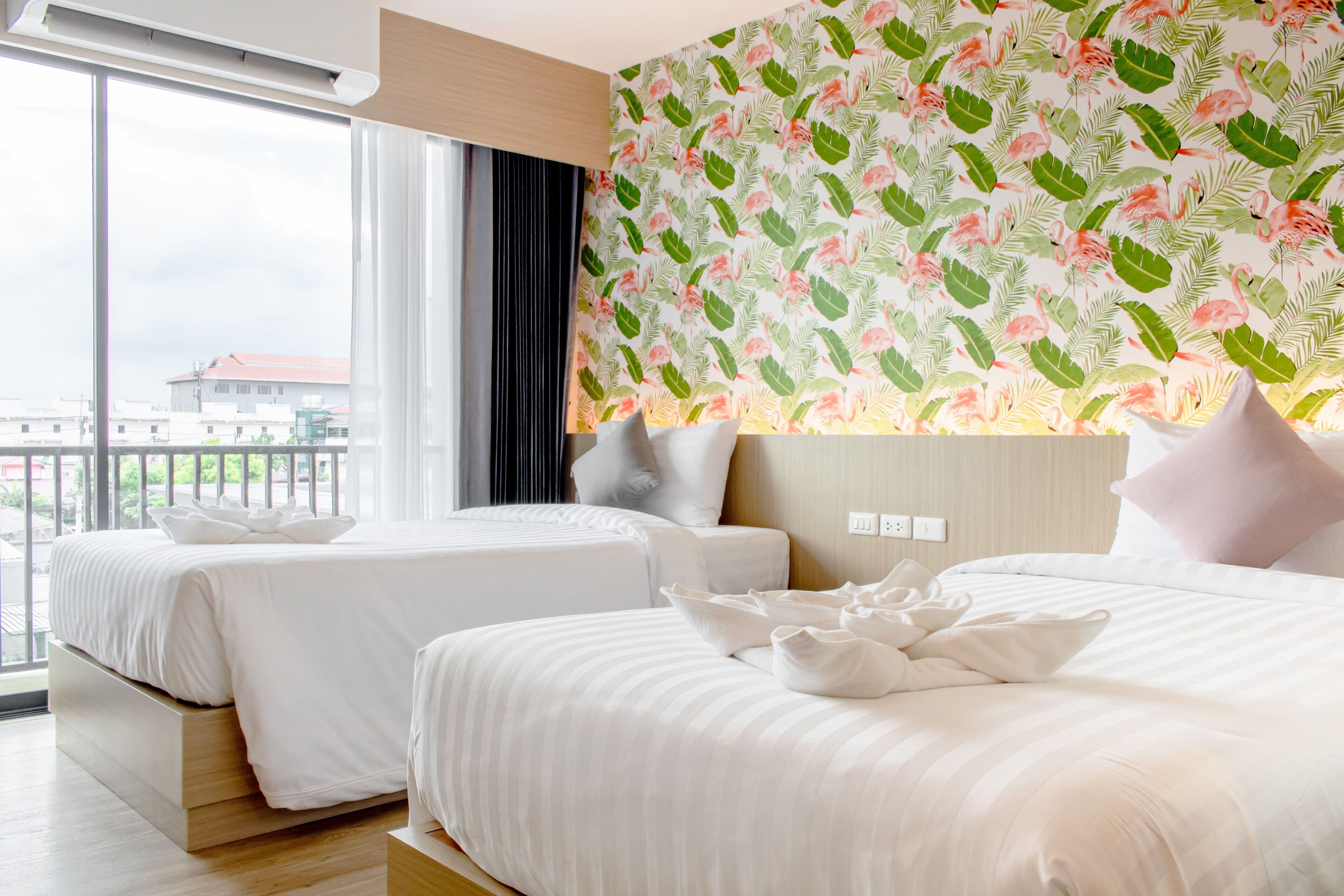 A hotel room with two beds, a large window, and a floral wallpaper.