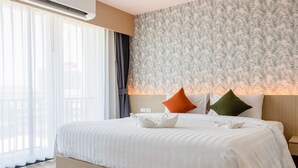 A hotel room with a large bed, white bedding, a patterned wall, and a view through sheer curtains. - ONE Hotel (Khlong Luang)