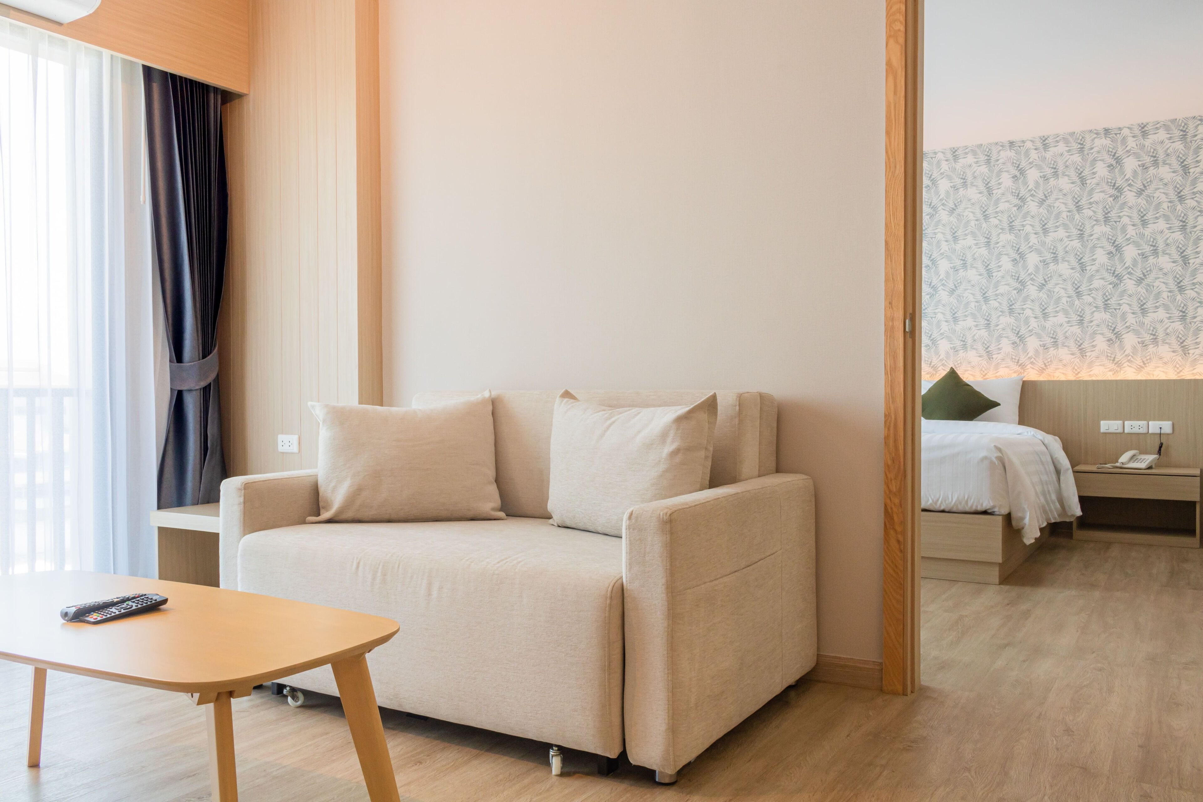 Una habitación de hotel moderna con sofá, una mesita, una mesita de noche con lámpara y un papel tapiz estampado en la pared.