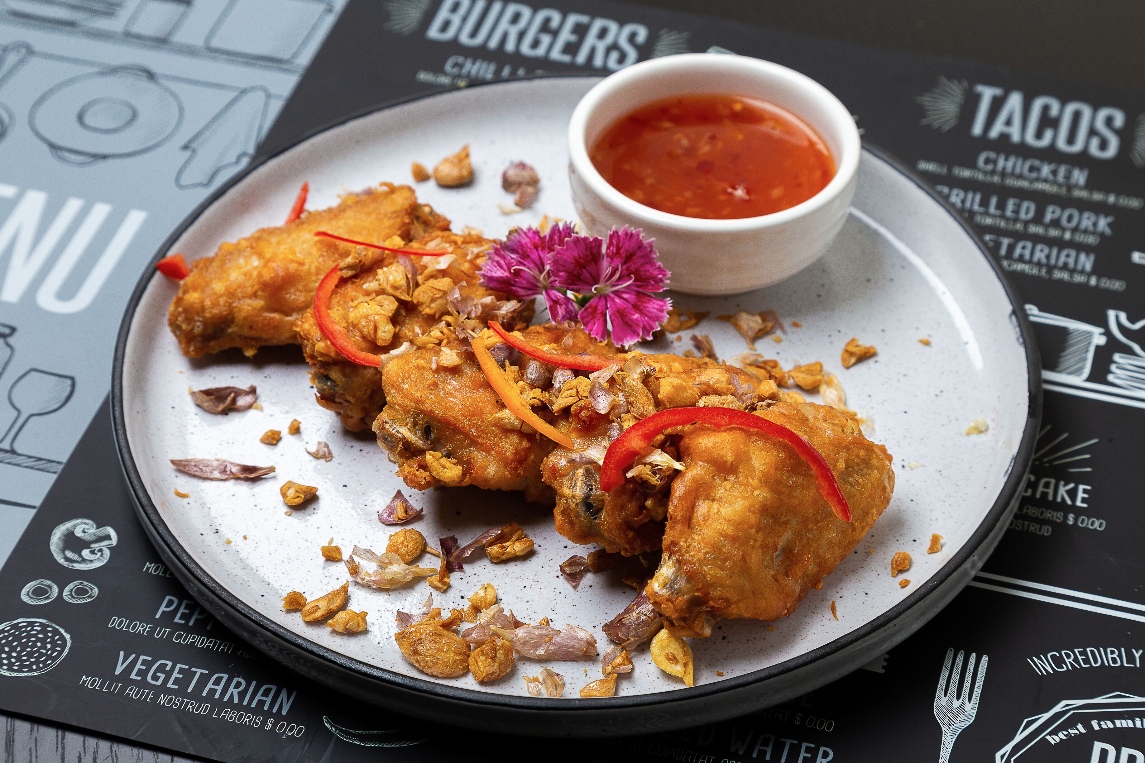 Un plato de pollo frito con adornos y una salsa al lado, sobre una mesa con un menú de fondo.