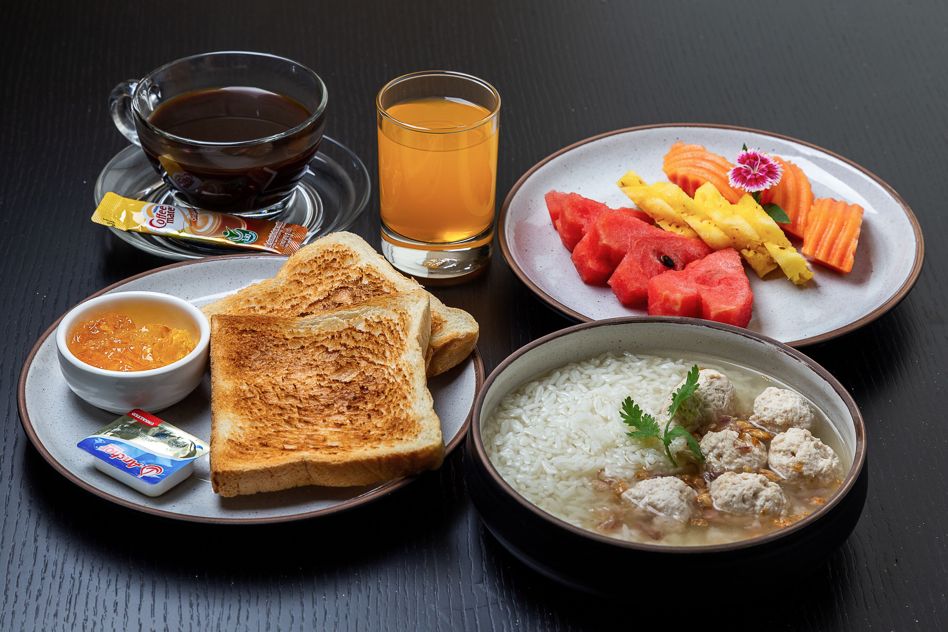 A meal consisting of toast, soup, rice with meatballs, and a plate with watermelon and carrot slices.