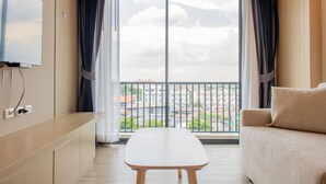 A modern hotel room with a large window, a sofa, a small table, and a TV mounted on the wall. - ONE Hotel (Khlong Luang)