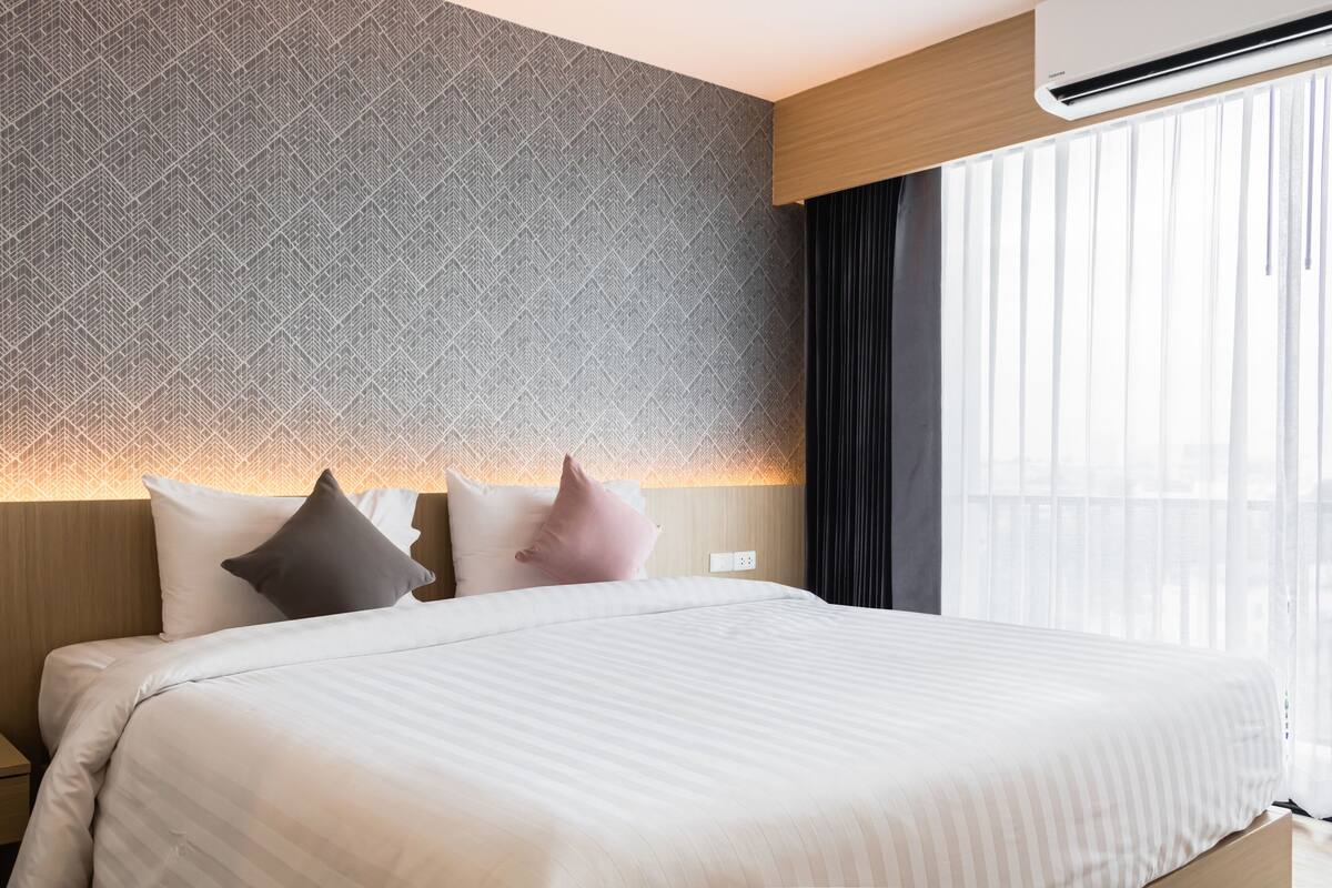 Una habitación de hotel con una cama grande, un papel tapiz decorado y una ventana con cortinas.